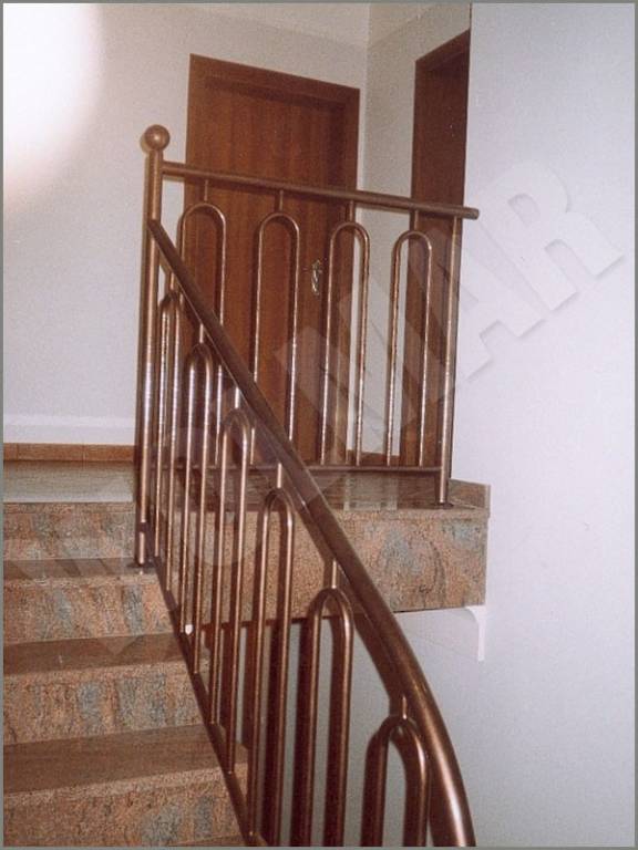 Poręcz schodowa malowana proszkowo na tle drzwi drewnianych mocowana do marmurowych schodów